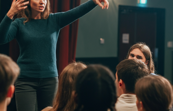 A speaker engages with an audience in a theatre setting.